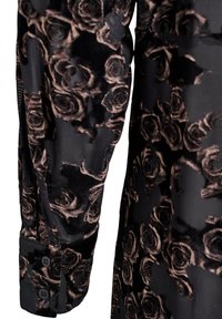 Črna tkanina z subtilnim vzorcem vrtnic v temnih tonih. Ima manšeto z gumbi in teksturirano površino, ki združuje mehak žamet in gladek material.