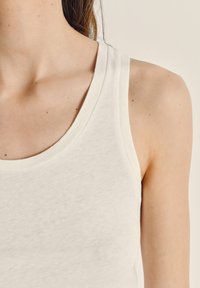 Valge puuvillane tank top, millel on pehme tekstuur, laiad rihmad ja ümmargune kaelus, esitledes lihtsat ja klassikalist disaini.