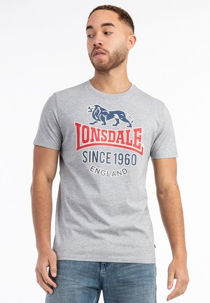Grijze t-shirt met korte mouwen, voorzien van een blauw leeuwgraphic en rode tekst "Lonsdale Since 1960 England" op de voorkant. Casual pasvorm.