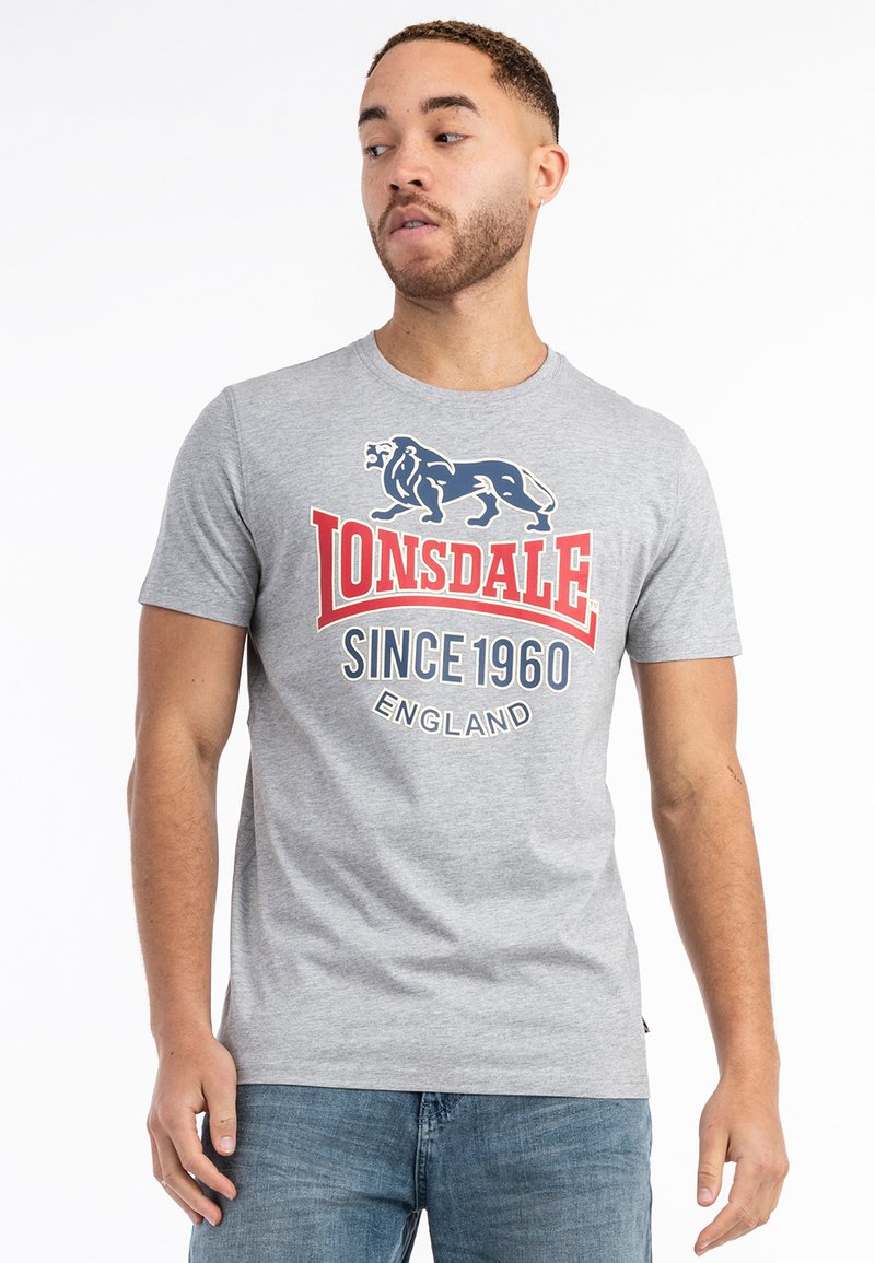 Grå kortærmet t-shirt med et blåt løvegrafik og rød tekst "Lonsdale Since 1960 England" på fronten. Casual fit.