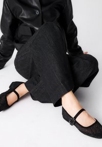 Pantalones de mezclilla negros con corte recto y costuras naranjas en contraste, combinados con zapatos negros texturizados que tienen una correa y hebilla.