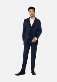 Marineblauer Dreiteiler aus strukturiertem Stoff, bestehend aus einem einreihigen Sakko, einer Weste und schmal geschnittenen Hosen, kombiniert mit einem weißen Hemd.