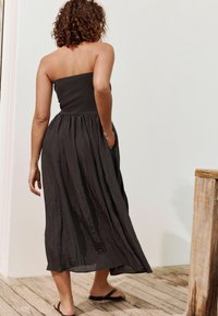 Robe noire sans bretelles avec un bustier ajusté, une jupe plissée fluide et des poches latérales. Fabriquée en tissu léger, elle présente une surface texturée.