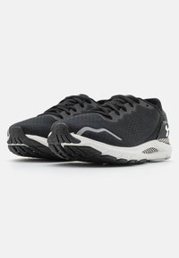 Zwarte sportschoenen met een bovenwerk van mesh, een gestructureerd patroon, witte accenten en een gewatteerde witte zool met een zwarte profielonderzijde.