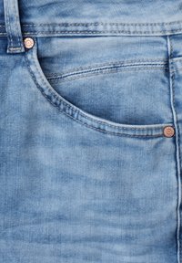 Zbliżenie na jasnoniebieskie jeansy denim, pokazujące przednią kieszeń, podwójne przeszycia, szlufkę na pasek i metalowe nity na materiale.