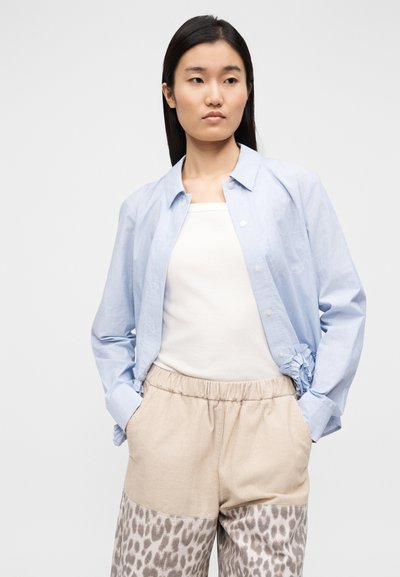 Ανοιχτό μπλε ριγέ πουκάμισο με κουμπιά και γυρισμένα μανίκια, συνδυασμένο με μπεζ και γκρι παντελόνι με μοτίβο λεοπάρ.