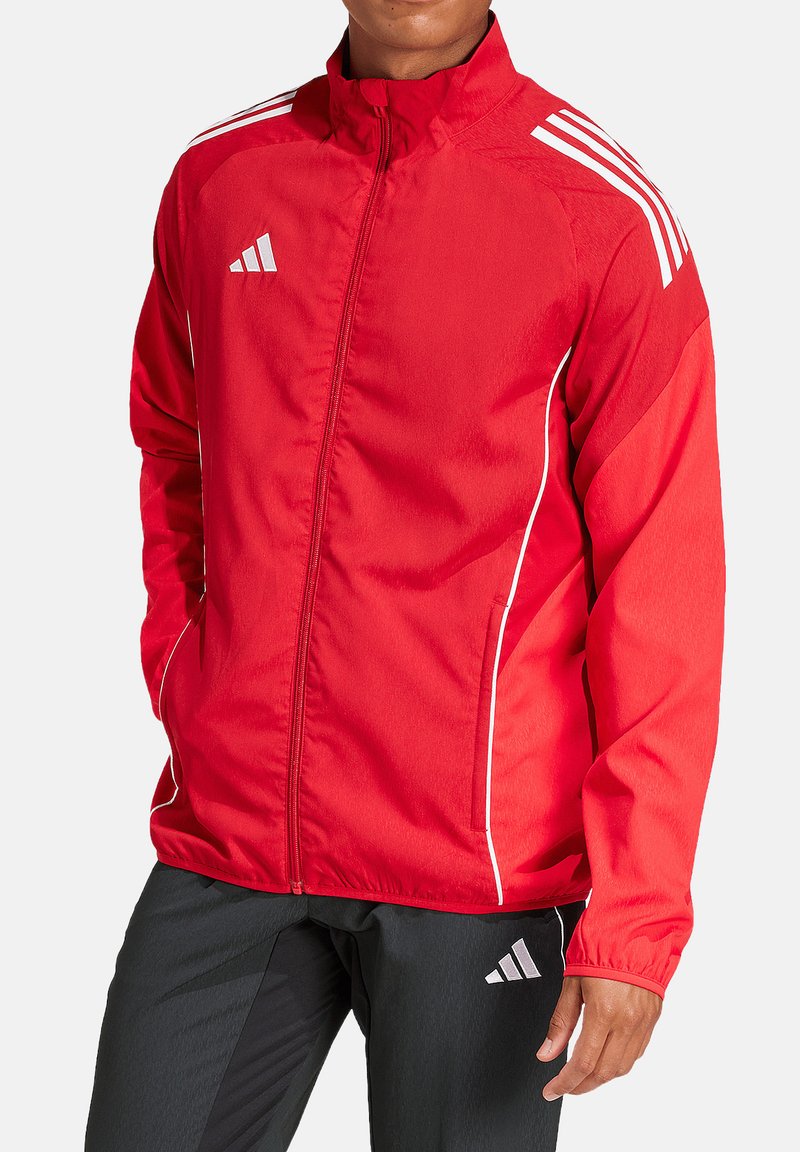 Rode sportjack met een ritssluiting aan de voorkant, witte accenten, en drie witte strepen op de schouders, gemaakt van lichtgewicht stof.