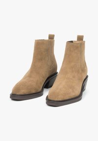 Tan suede ankle boots with a pointed toe, elastic side panels, and a low stacked heel. Features a smooth texture and minimalist design.