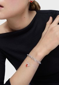 Pulsera de cadena de plata con un acento de gema roja, llevada en una muñeca. Un diseño de cadena simple e interconectada realza una apariencia elegante.
