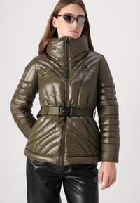Puffer jacket in olive green, featuring a high collar, diagonal stitching, and a belted waist. The fabric is shiny and quilted.