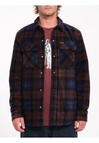 Langærmet flannelskjorte i marmor, sort og blå plaid mønster; har to frontlommer og trykknaplukninger. Bæres over en marmor grafisk t-shirt.