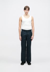 Hvitt ermeløst tanktop kombinert med mørk marineblå vide bukser og svarte sko. Outfitet har en avslappet passform og minimalistisk design.