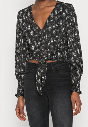 Blusa nera con bottoni, decorata con un motivo floreale bianco, scollatura a V profonda, maniche lunghe con polsini arricciati e dettaglio anteriore annodato.