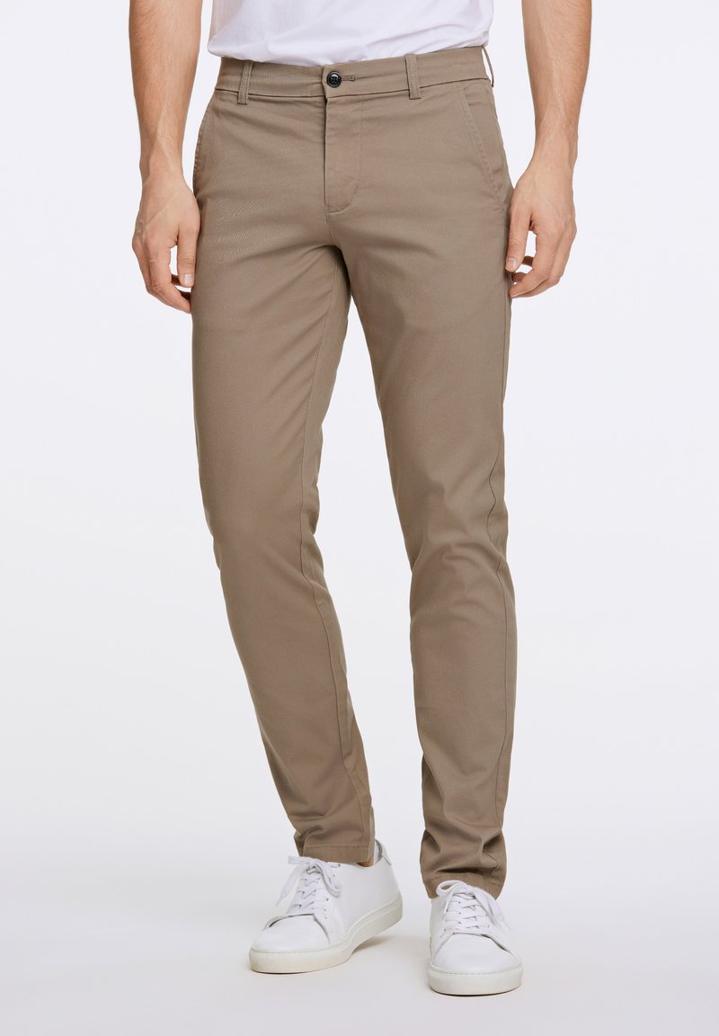 Beige, slim fit chino nadrág, pamut keverékből készült, gombos záródással, elülső zsebekkel, és a fehér sportcipő felett végződő szegéllyel.