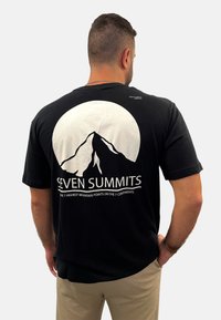 Schwarzes Baumwoll-T-Shirt mit einer weißen Bergsilhouette, kreisförmigem Hintergrund und dem Text "SEVEN SUMMITS" mit ergänzenden Details darunter.