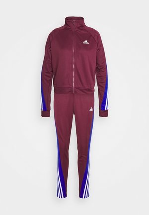 Vinrød Adidas træningsdragt med lynlåstrøje og tilhørende bukser, med blå og hvide striber på ærmer og ben, Adidas-logoer på bryst og lår.