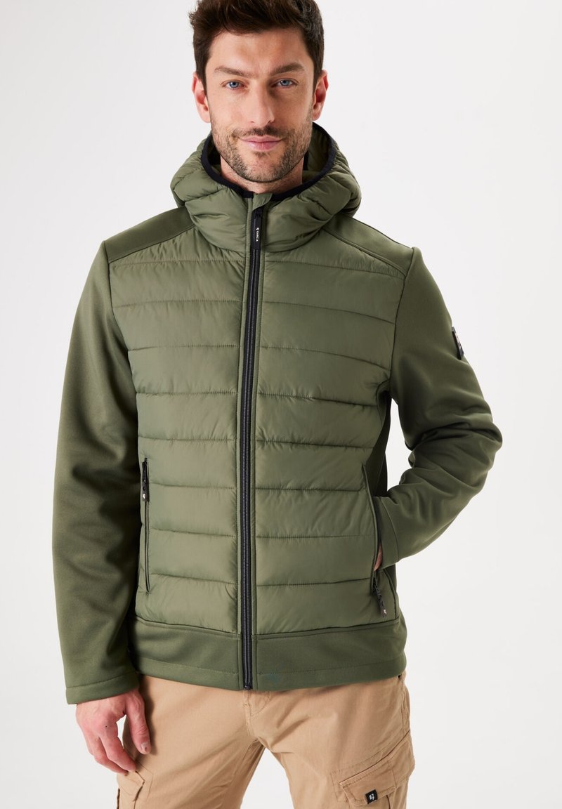 Doudoune vert olive avec fermeture éclair devant et capuche, présentant une texture matelassée et des poches latérales. Tissu durable avec une finition lisse.