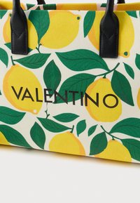 Καμβαδένια τσάντα ώμου με μοτίβο λεμονιού και φύλλων. Μαύρο δερμάτινο χερούλι και τυπωμένο λογότυπο "VALENTINO" με έντονα γράμματα. Φωτεινός, πολύχρωμος σχεδιασμός.