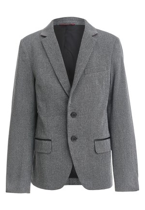 Personne portant un blazer gris avec des coudières noires, un T-shirt graphique noir, un jean bleu et des baskets montantes noires avec des lacets rouges.