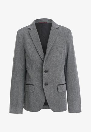 Personne portant un blazer gris avec des coudières noires, un T-shirt graphique noir, un jean bleu et des baskets montantes noires avec des lacets rouges.