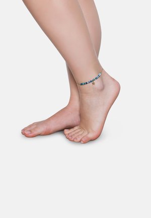 Tobillo con una pulsera de cuentas multicolores y un charm de estrella, llevada en un tobillo desnudo. Las cuentas incluyen tonos de azul, púrpura y dorado, colocadas sobre una cadena delgada.