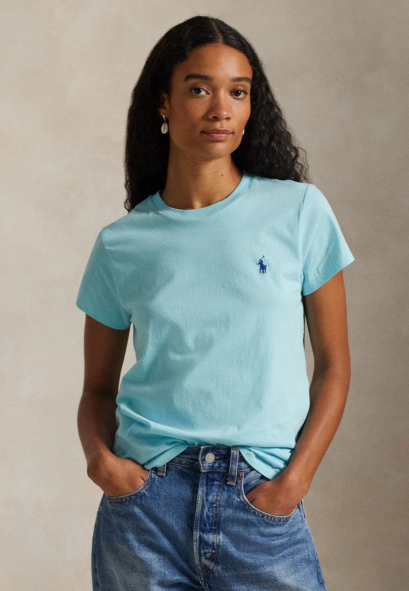 Ανοιχτό μπλε βαμβακερό T-shirt με κοντά μανίκια και στρογγυλή λαιμόκοψη· διαθέτει μικρό, σκούρο μπλε κεντητό λογότυπο στο στήθος.