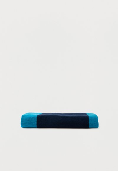 Serviette pliée avec des rayures horizontales alternées larges bleu foncé et turquoise vif sur un fond clair uni.