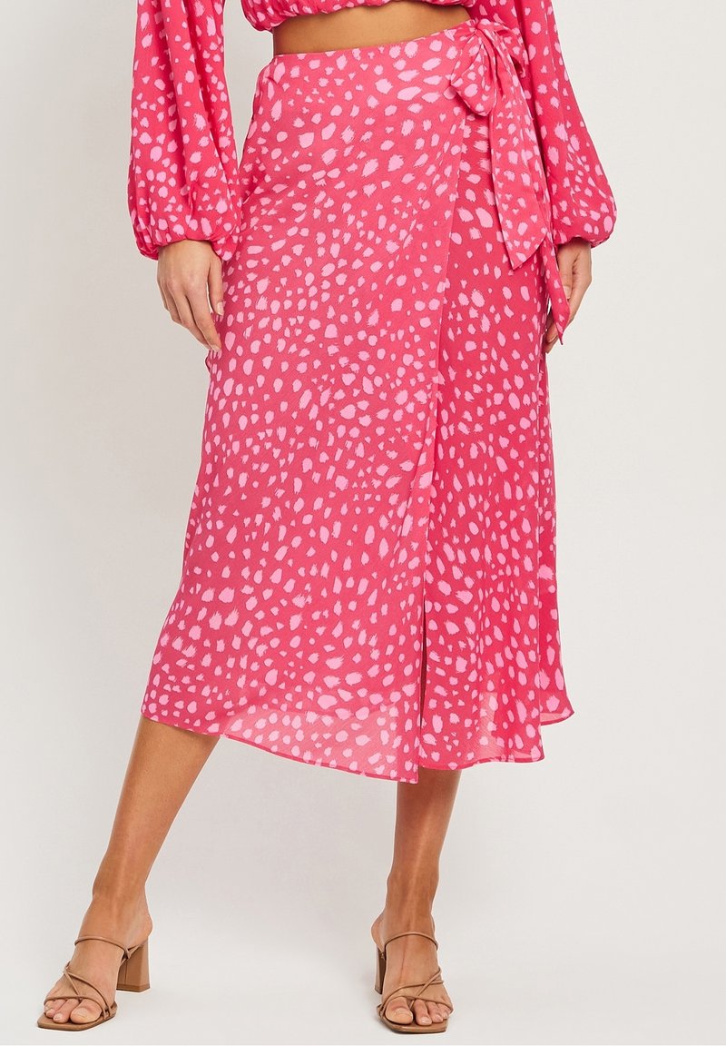 Růžová zavinovací sukně s nepravidelnými bílými skvrnami, vyrobená z lehkého materiálu. Má zavázaný pas a volnou siluetu, délka ke kolenům.