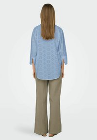 Cămașă albastră deschisă cu model broderie anglaise, croială lejeră, mâneci până la trei sferturi, asortată cu pantaloni bej texturat și lejeri.