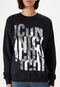 Sudadera negra hecha de mezcla de algodón. Presenta un gran texto metálico plateado con textura desgastada. Puños y dobladillo acanalados. Ajuste casual.