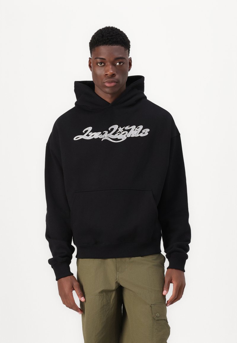 Sudadera negra con capucha y bolsillo frontal, con diseño de logotipo en script plateado. Puños y dobladillo de canalé, textura de tela suave.