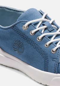 Sneaker in tessuto azzurro chiaro con suola in gomma bianca, caratterizzato da occhielli metallici, lacci bianchi e un logo impresso sul lato.