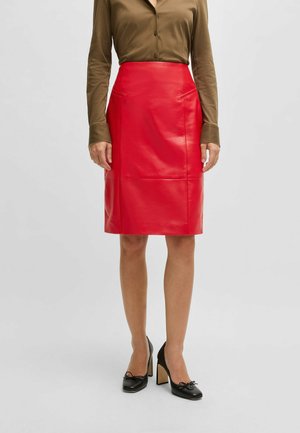 Rode leren kokerrok met een hoge taille, twee zijzakken en een slanke, gladde textuur. Gecombineerd met een bruine blouse met knopen en zwarte hakken.