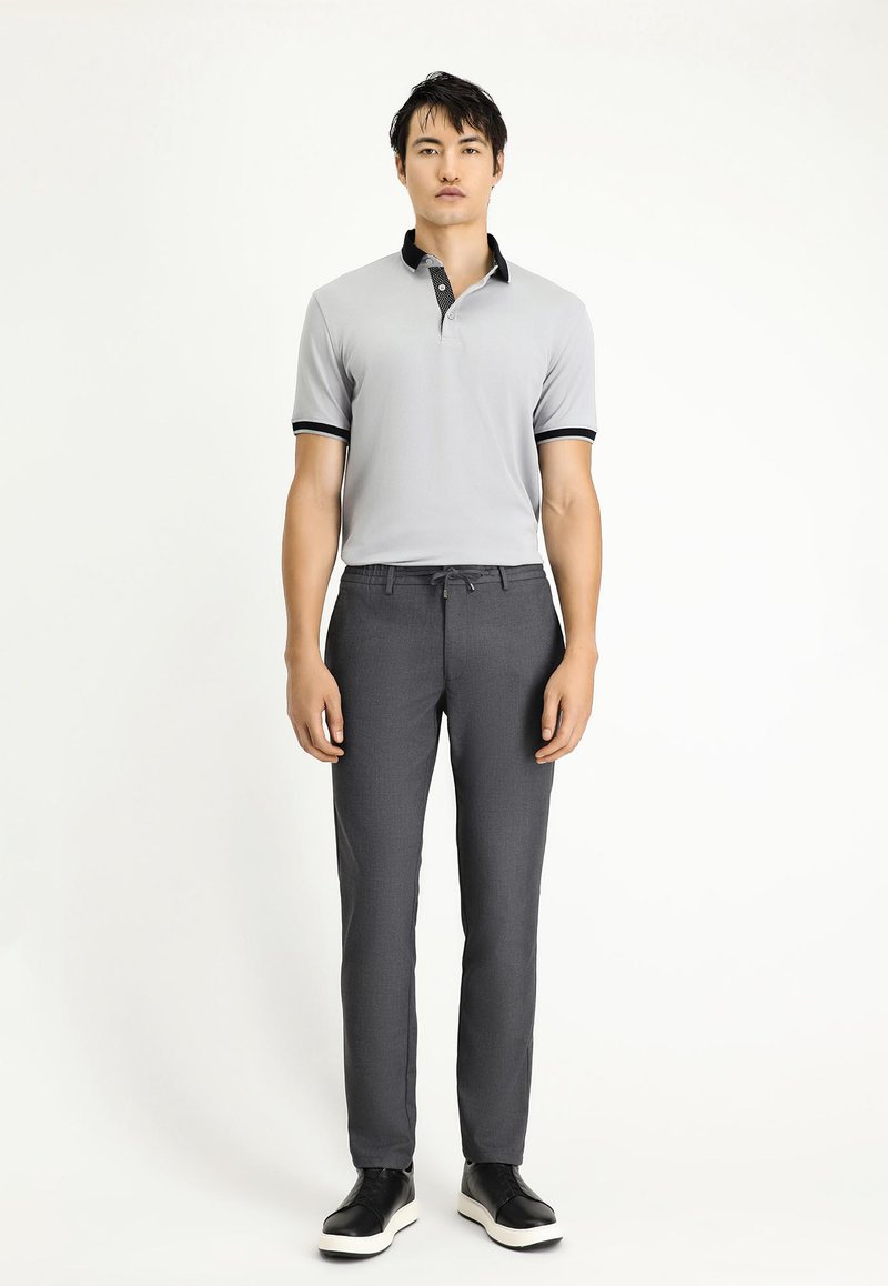 Grijze polo met zwarte kraagaccenten, in combinatie met grijze op maat gemaakte broeken en zwarte sneakers. Gladde stof, getailleerd ontwerp en minimalistische stijl.