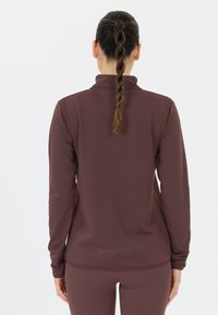 Pitkähihainen, slim fit -paita rikkaita burgundin sävyissä, jossa on korkea kaulus ja peukaloreiät. Huomattava ommeltu yksityiskohta helmassa.
