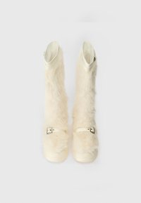 Bílé boty z umělé kožešiny s hladkou gumovou podrážkou, vybavené plochým přezkovým páskem a úzkým otvorem nahoře pro snadné obutí.