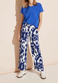 Blå V-hals t-shirt i kombination med vida byxor med ett marinblått och vitt ikat-mönster, kompletterat med ljusa sneakers.