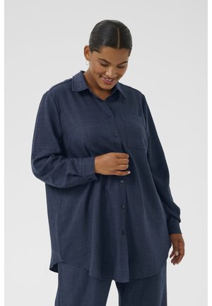 Chemise bleu foncé à boutons en tissu texturé, avec un col, des manches longues, une poche sur la poitrine et un ourlet arrondi.