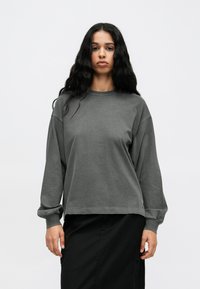 Szary, długi sweatshirt z luźnym fasonem, okrągłym dekoltem i ściągaczami na rękawach. Posiada teksturowane wykończenie oraz subtelne detale w szyciu.