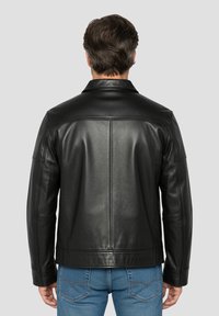 Zwarte leren jas met een gestructureerd ontwerp, voorzien van een kraag en zichtbare stikseldetails, gedragen met blauwe spijkerbroek, gezien vanaf de achterkant.