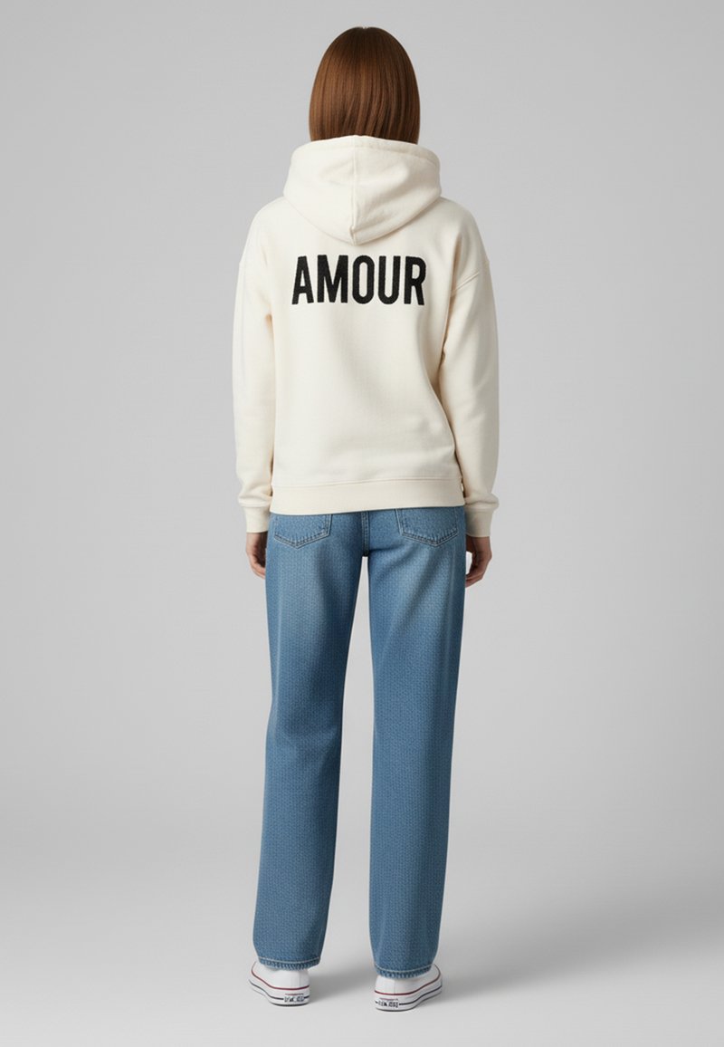 Felpa crema con la scritta "AMOUR" stampata in nero sulla schiena, abbinata a jeans leggeri blu con motivo e sneakers bianche con accenti rossi.