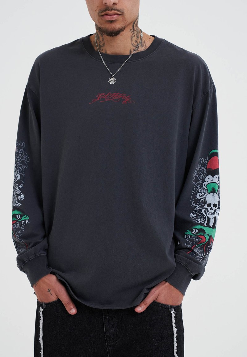 Dunkelgraues Langarmshirt mit rotem Grafiktext auf der Brust und aufwendigen Ärmeln, die Farben, Schädel, Muster und Schlangen-Motive zeigen.