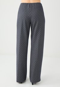 Patroon gebreide wijde broek in marineblauw, met een geometrisch patroon in wit en lichtblauw. Gemaakt van een zachte, lichte stof.
