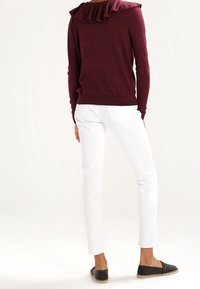 Suéter burdeos con escote con volantes, pantalones ajustados blancos y alpargatas negras. Tejido suave, corte ajustado y acentos sencillos.