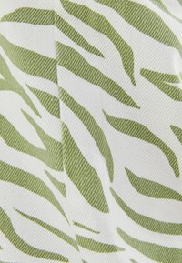 Vitt tyg med ett mönster av gröna löv i ett zebramönster, med strukturerad yta och böjda linjer genom hela.