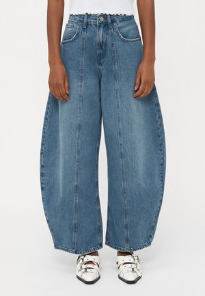 Lyseblå, bredbenede denim jeans med højt liv, der har forlommer og en falmet finish. Sammen med hvidt fodtøj.