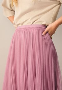 Jupe en tulle plissé rose clair avec une taille élastique, présentant une texture douce et transparente ainsi qu'un design fluide.