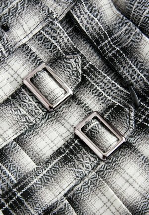 Schwarzes und weißes Karomuster aus Stoff mit silbernen quadratischen Schnallen, sichtbaren Nähten und einer weichen Textur, die ein monochromes kariertes Muster einfängt.