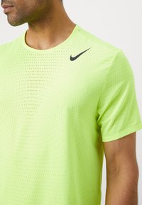 Koszulka sportowa z krótkim rękawem Nike w fluorescencyjnym zielonym kolorze, z teksturowanym, perforowanym materiałem, okrągłym dekoltem oraz czarnym logo swoosh na lewej piersi.