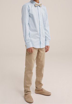 Light blue button-up shirt with small dark polka dots, paired with beige chinos and beige moccasin-style shoes. Bow tie adds detail.